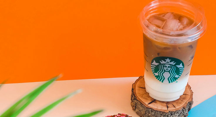 Iced coffee on wooden coaster with orange background.