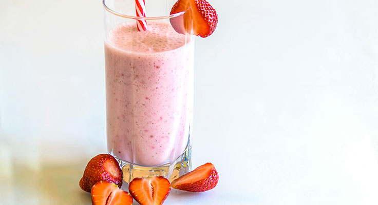 Fresh strawberry smoothie in glass with sliced berries.