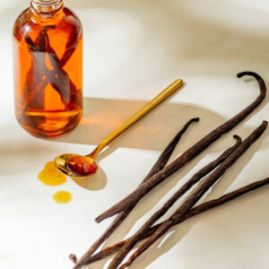 Vanilla extract in bottle with vanilla pods and spoon.