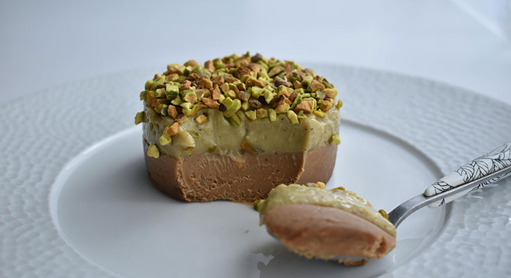 Pistachio-topped chocolate dessert on plate with spoon.