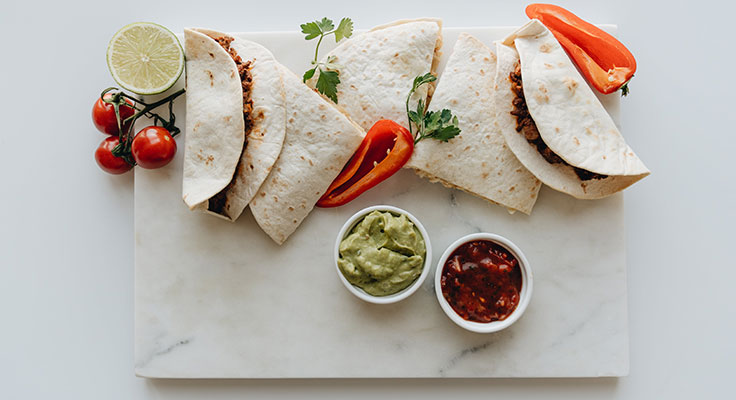 Fresh tacos with guacamole and salsa on marble.