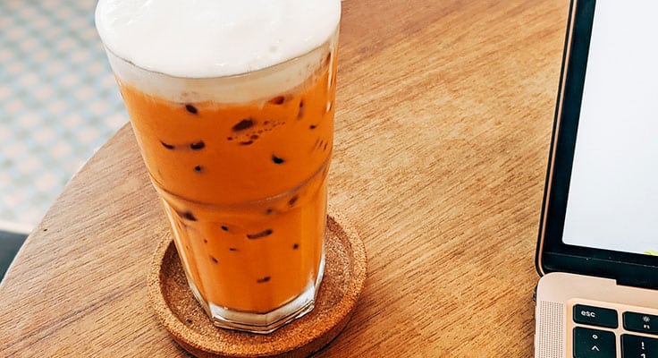 Iced Thai tea on desk near laptop.