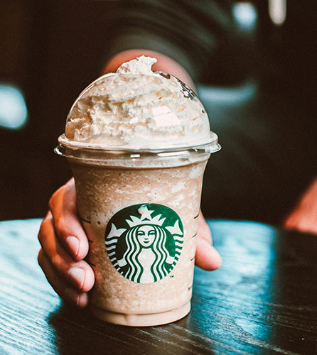 Hand holding a Starbucks Frappuccino on a table.