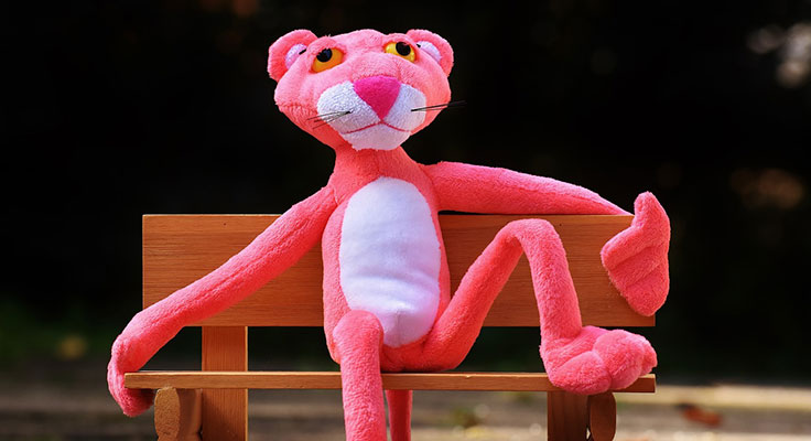 Pink plush panther toy sitting on wooden bench.