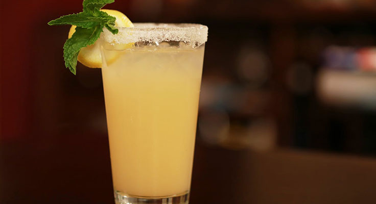 Lemon cocktail with mint garnish in glass.