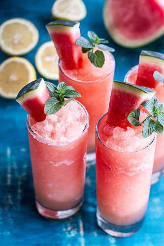 Watermelon slushies with mint garnish on blue background.