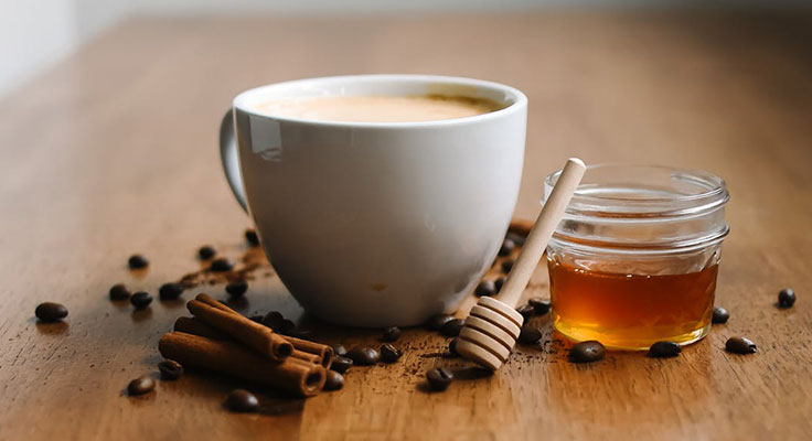 Coffee cup, honey jar, coffee beans, and cinnamon sticks.