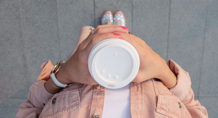 Person holding coffee cup, pink jacket, fashionable outfit.