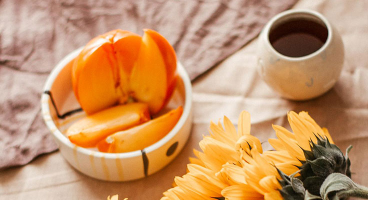 Fresh persimmon slices, tea, and sunflowers on table.