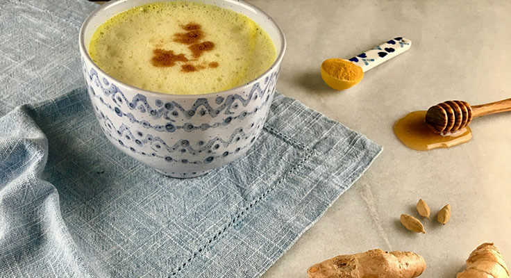 Turmeric latte in patterned cup, ginger, honey dipper.