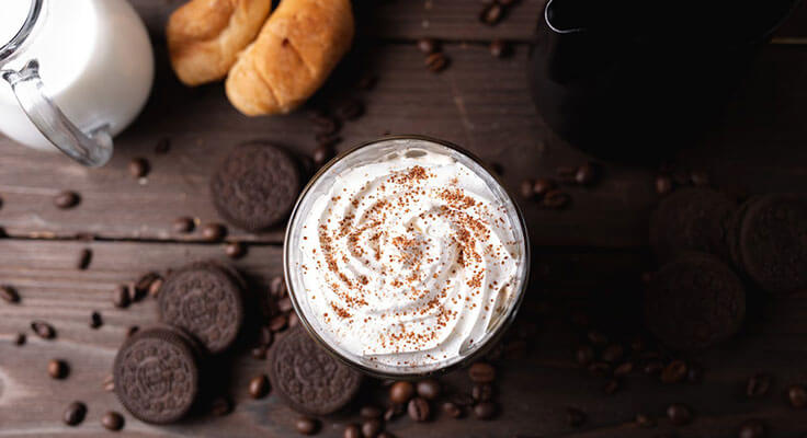 Whipped cream-topped coffee with cookies and croissants.