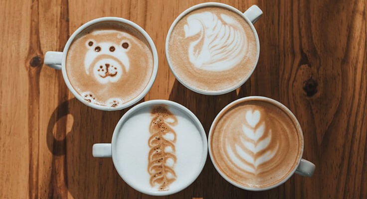 Artistic latte coffee designs on wooden table.