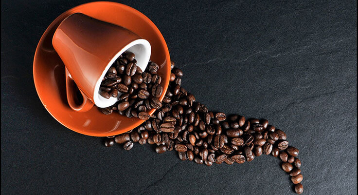 Spilled coffee beans from overturned cup on dark surface.