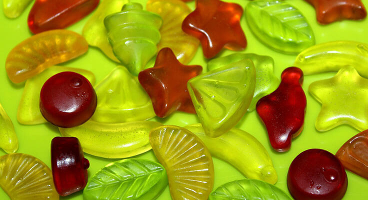 Assorted colorful gummy candies on green background.