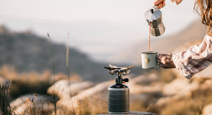 Person pouring coffee outdoors camping.