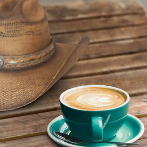 Cowboy hat and latte art coffee on wooden table.