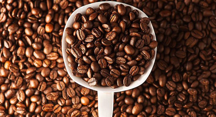 Scoop of roasted coffee beans on beans background.