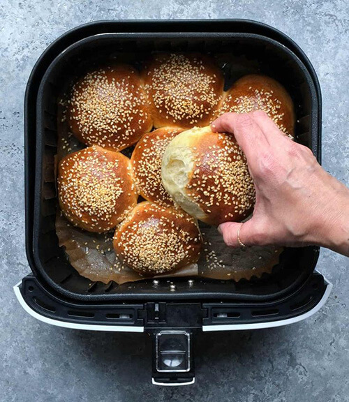 Hand removing sesame bun from air fryer.