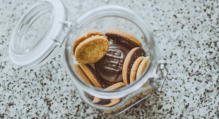 Assorted cookies in a glass jar on speckled countertop.