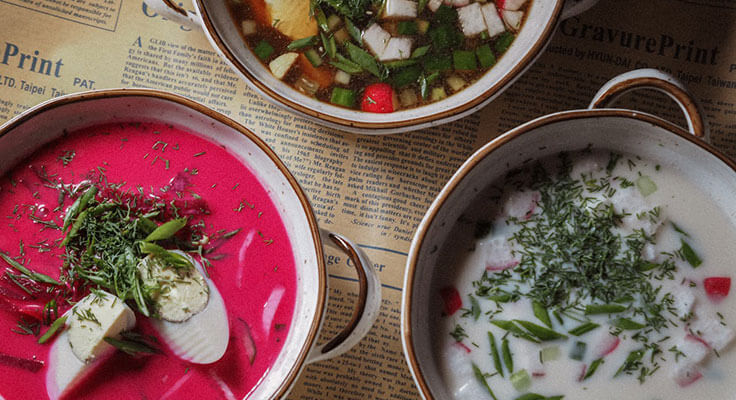 Three bowls of colorful soup on printed paper.