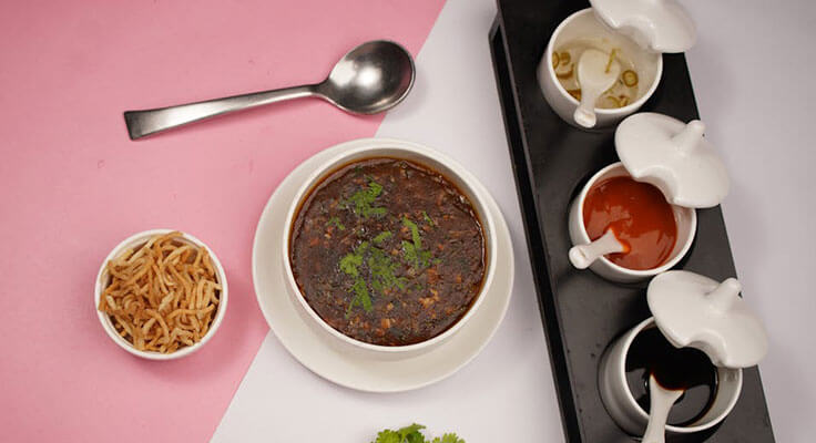 Overhead view of manchow soup with fried noodles and condiments.