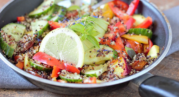 Colorful quinoa vegetable stir-fry with lemon garnish.