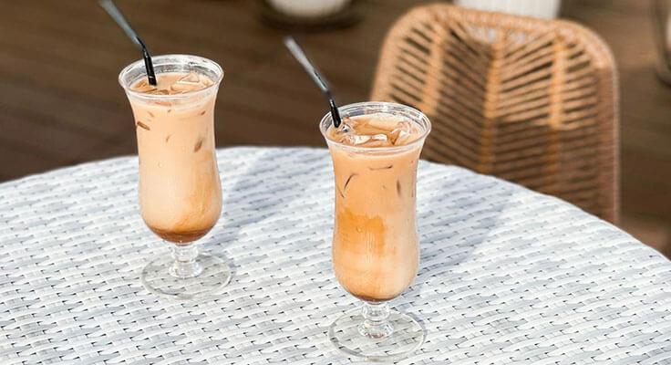 Two iced lattes on outdoor wicker table.