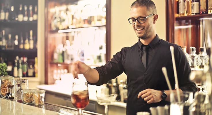 Smiling bartender serving cocktail at bar counter.