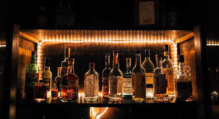Illuminated liquor bottles on bar shelf at night.