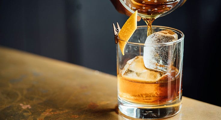 Whiskey poured over ice in glass with orange peel.