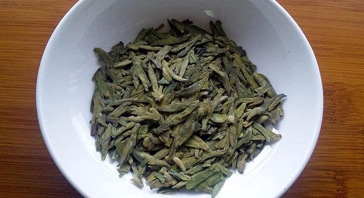 Loose green tea leaves in a white bowl.