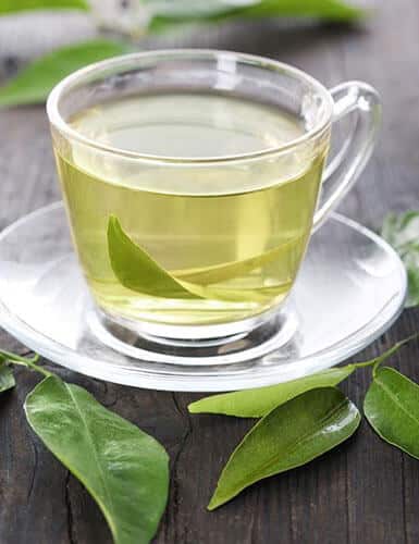 Cup of green tea with leaves on wooden surface.
