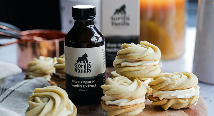 Vanilla extract bottle with frosted cookies on table.