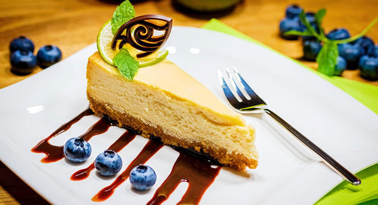 Slice of cheesecake with blueberries and chocolate garnish.
