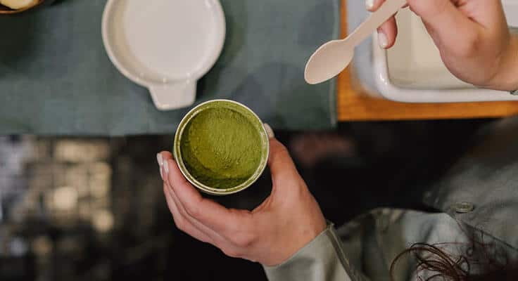 Person holding matcha tea cup with spoon.