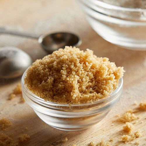 Brown sugar in clear bowl with measuring spoon.