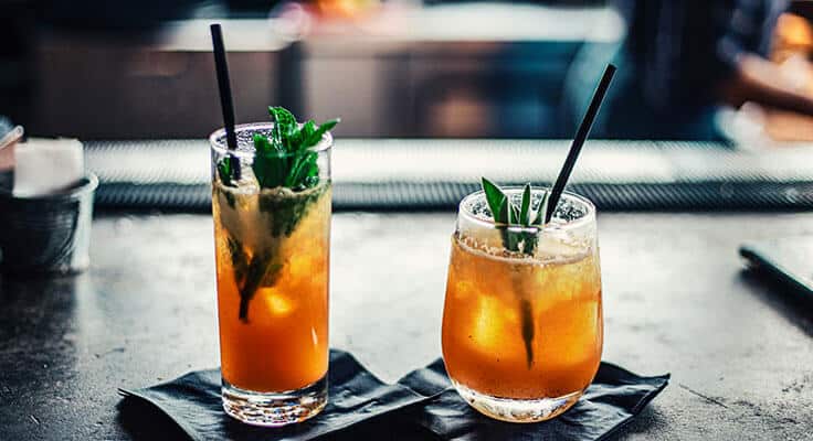 Two cocktails on bar counter with mint garnish.