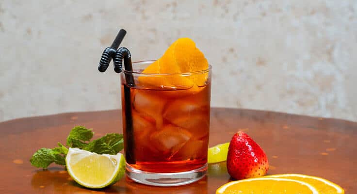 Iced cocktail with citrus garnishes on wooden table.