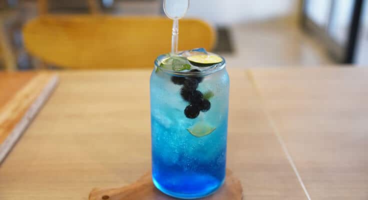 Blue cocktail with lime on wooden table.
