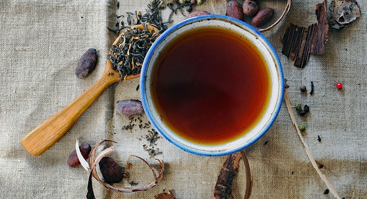 Cup of tea with loose leaves and spices on fabric.