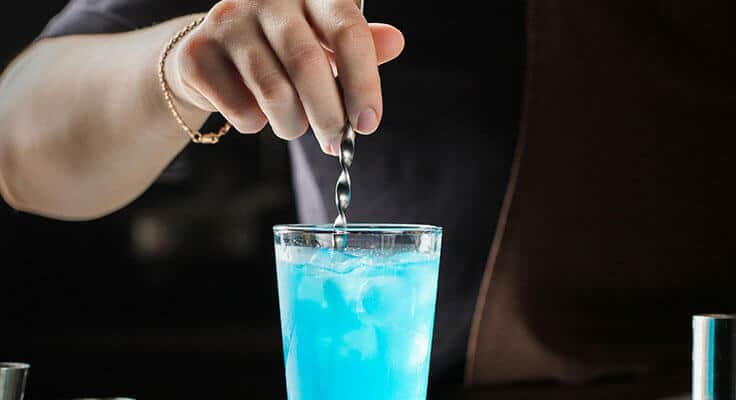 Bartender stirring blue cocktail with ice.