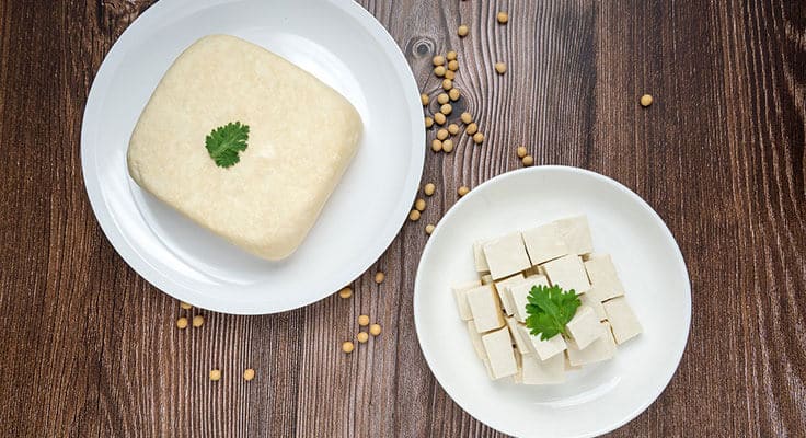 White plate with tofu blocks on wood surface.
