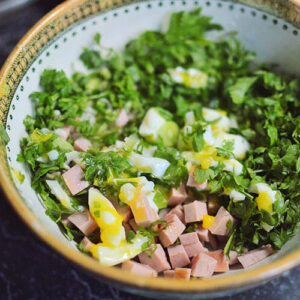 Bowl of salad with eggs, ham, and fresh herbs.