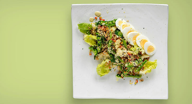 Quinoa salad with egg slices on white plate.