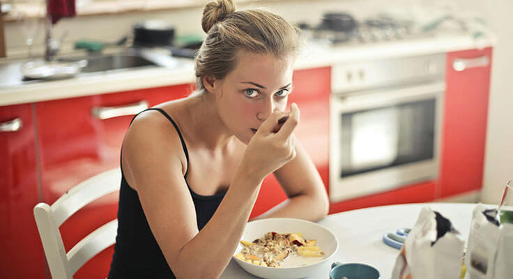 Woman eating breakfast in a red kitchen.