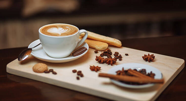 Latte art coffee, cookies, and spices on wooden serving board.