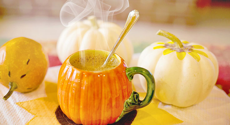 Steaming beverage in pumpkin-shaped mug with autumn decor.
