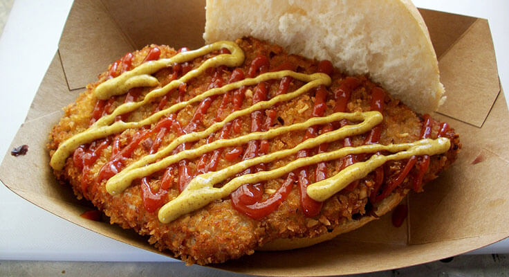 Breaded pork tenderloin sandwich with ketchup and mustard.