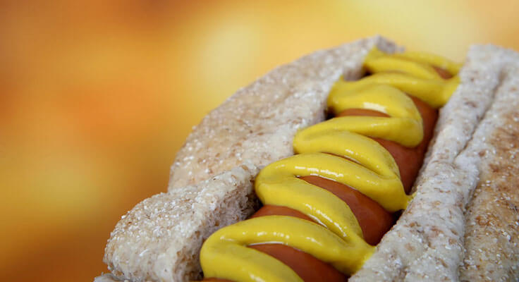Hot dog with mustard on whole grain bun.