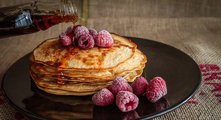Stack of pancakes with raspberries and syrup pouring.